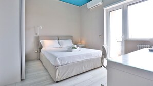 A bedroom with a bed, bedside table, lamp, and a window with a view. - GuestHost - Vento di Mare House (Naples)