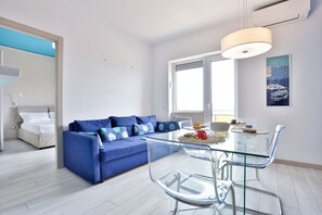 Ein modernes Wohnzimmer mit einem blauen Sofa, einem Glastisch und einem großen Fenster.
