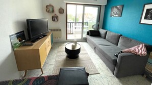 Una sala de estar con televisor, sofá y vistas al exterior.