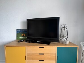 Ein Fernseher auf einer Holzkombination mit Schubladen, einer Fernbedienung, einem Buch und einer Vintage-Lampe.
