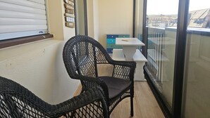 Un balcón con sillas de mimbre, una mesita y vistas a edificios.