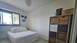 Un dormitorio con cama, ventana, estante con cestas y alfombra tejida.