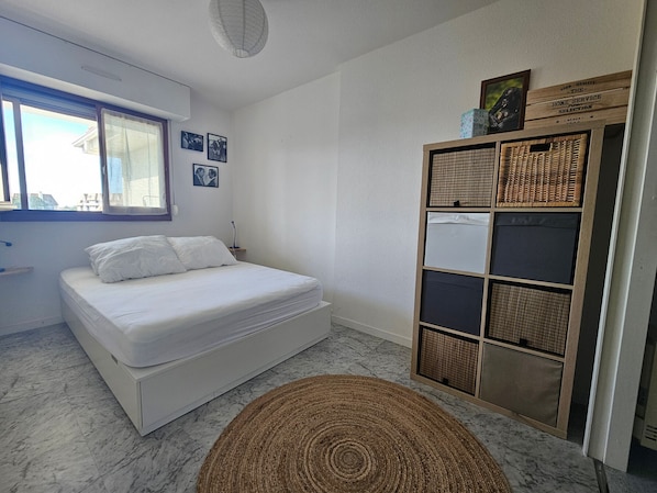 Ein Schlafzimmer mit einem Bett, einem Fenster, einer Wandablage mit Körben und einem gewebten Teppich.