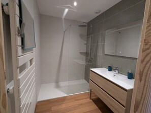 Un bagno moderno con cabina doccia in vetro, lavabo bianco con mobile in legno e uno specchio grande.