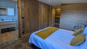 A modern bedroom with a wooden wall, a bed with a blue and white duvet, a wooden nightstand, and a bathroom with a mirror and sink.