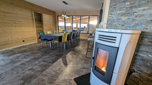 A modern kitchen with a wood-burning stove, a dining area with chairs and a table, and a large window providing natural light.