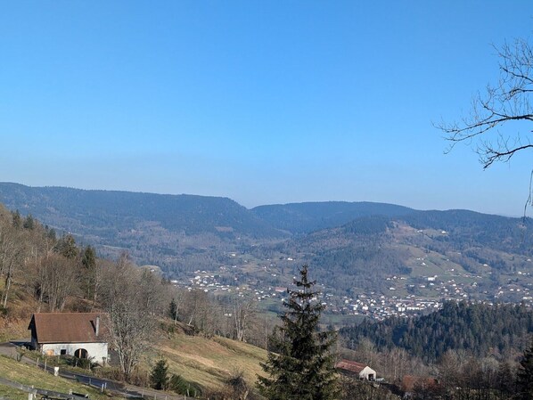 Paesaggio rurale con un piccolo edificio su una collina, circondato da alberi e una valle con case sparse.