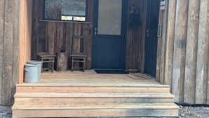 A wooden cabin with a dark blue door, a small window, and a set of wooden steps leading to the entrance.