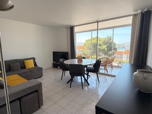 Ein modernes Wohnzimmer mit einer Couch, einem Esstisch mit Stühlen, einem Fernseher und einem Balkon mit Blick.