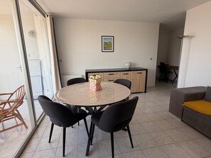 A dining area with a round table, four chairs, a kitchen in the background, and a sofa with a yellow cushion. - Ground floor T2 apartment, loggia, sea view in Banyuls-sur-Mer (Banyuls-sur-Mer)