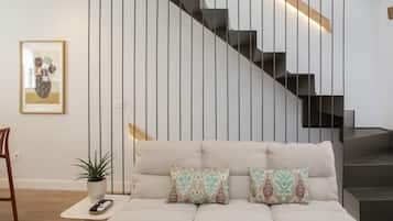Una sala de estar moderna con un sofá, una mesita con una planta, un cuadro enmarcado y una escalera.