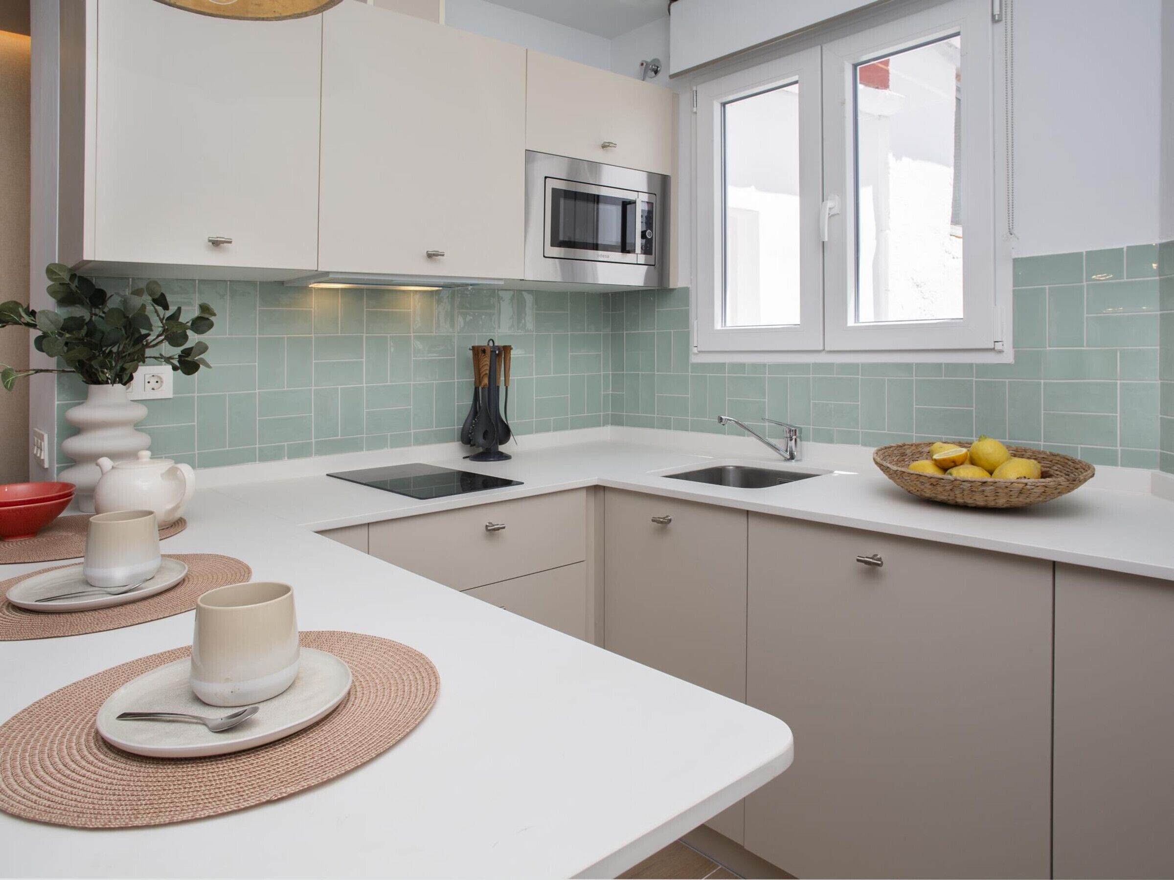 Een moderne keuken met witte kasten, een ingebouwde magnetron, een spoelbak en een raam.