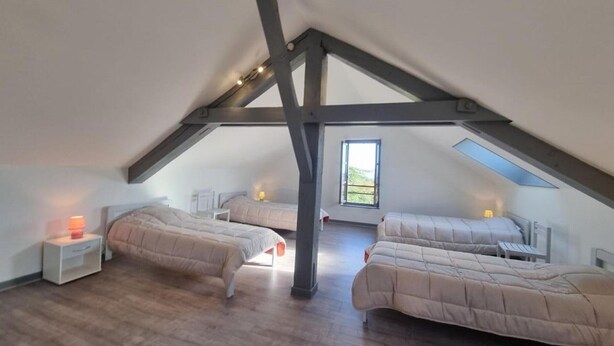 A spacious attic bedroom with three beds arranged in a U-shape, wooden flooring, and a skylight.