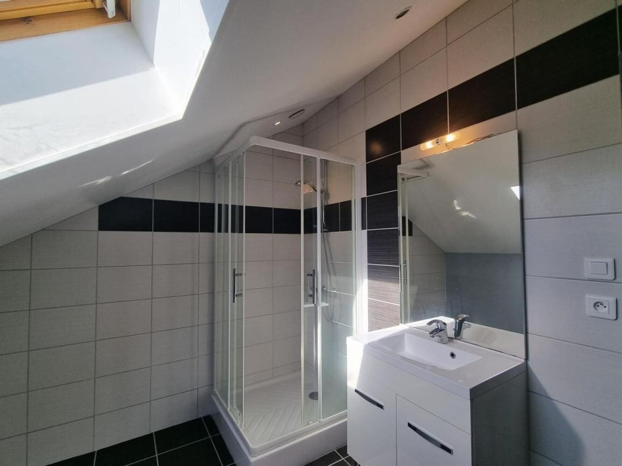 A modern bathroom with a skylight, a glass shower enclosure, and a white vanity with a mirror.