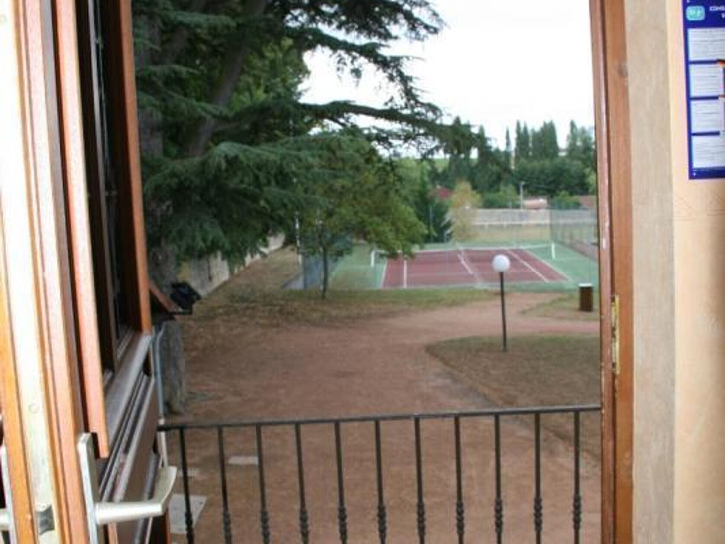 Uitzicht vanaf een balkon op een tennisterrein met bomen en een hek.