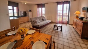 A compact living space with a kitchenette, a sofa, a dining table set for two, and a TV. - Family cottage in the heart of Côte Roannaise - Pets allowed (Saint-André-d'Apchon)