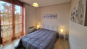 A bedroom with a bed, two bedside tables with lamps, a radiator, and a window with curtains. - Family cottage in the heart of Côte Roannaise - Pets allowed (Saint-André-d'Apchon)