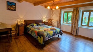 A bedroom with a wooden ceiling, a bed with a colorful floral bedspread, a nightstand with a lamp, and a window with curtains. - Spacious house with spa, ping-pong, and foosball, perfect for family relaxation (La Chapelle-aux-Bois)