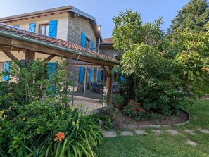 Une maison dotée d’un patio couvert, d’un jardin agrémenté de diverses plantes et fleurs, et d’une façade en pierre.