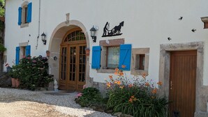 A building with a large wooden door, blue shutters, and a small garden with flowers. - Spacious house with spa, ping-pong, and foosball, perfect for family relaxation (La Chapelle-aux-Bois)