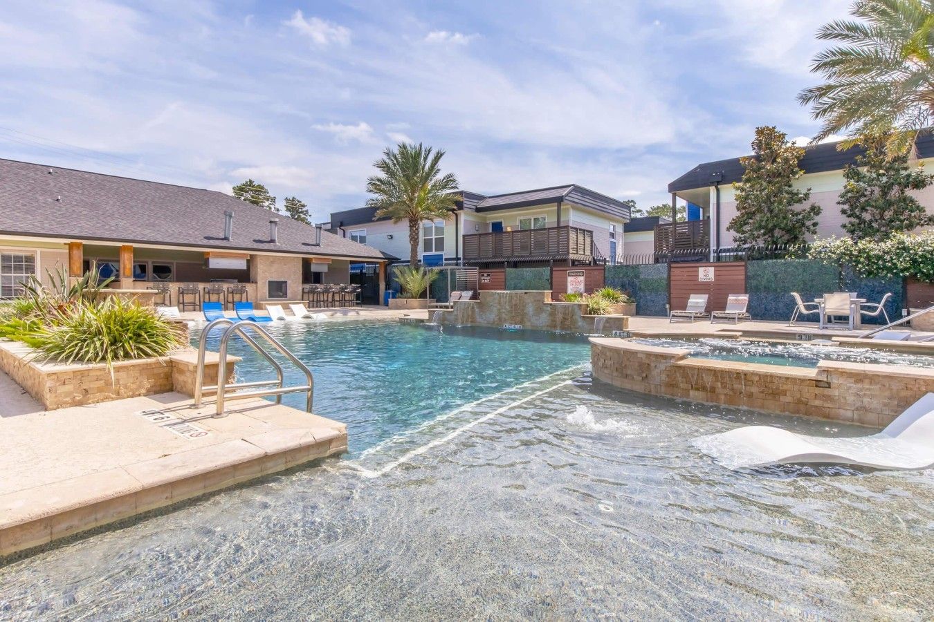 A swimming pool with a hot tub, lounge chairs, and a small waterfall feature.