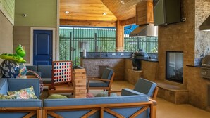 Una cocina moderna con una parrilla empotrada, un televisor montado sobre la encimera y un rincón de descanso con sofás azules y una mesa de centro de madera.