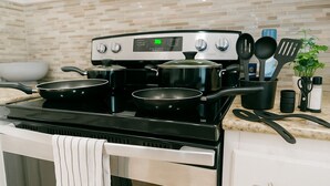 Una cocina con estufa, ollas, sartenes y utensilios.