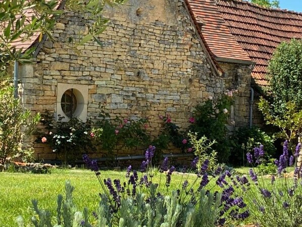 A stone building with a red-tiled roof, surrounded by a well-maintained garden with lavender and other flowering plants.