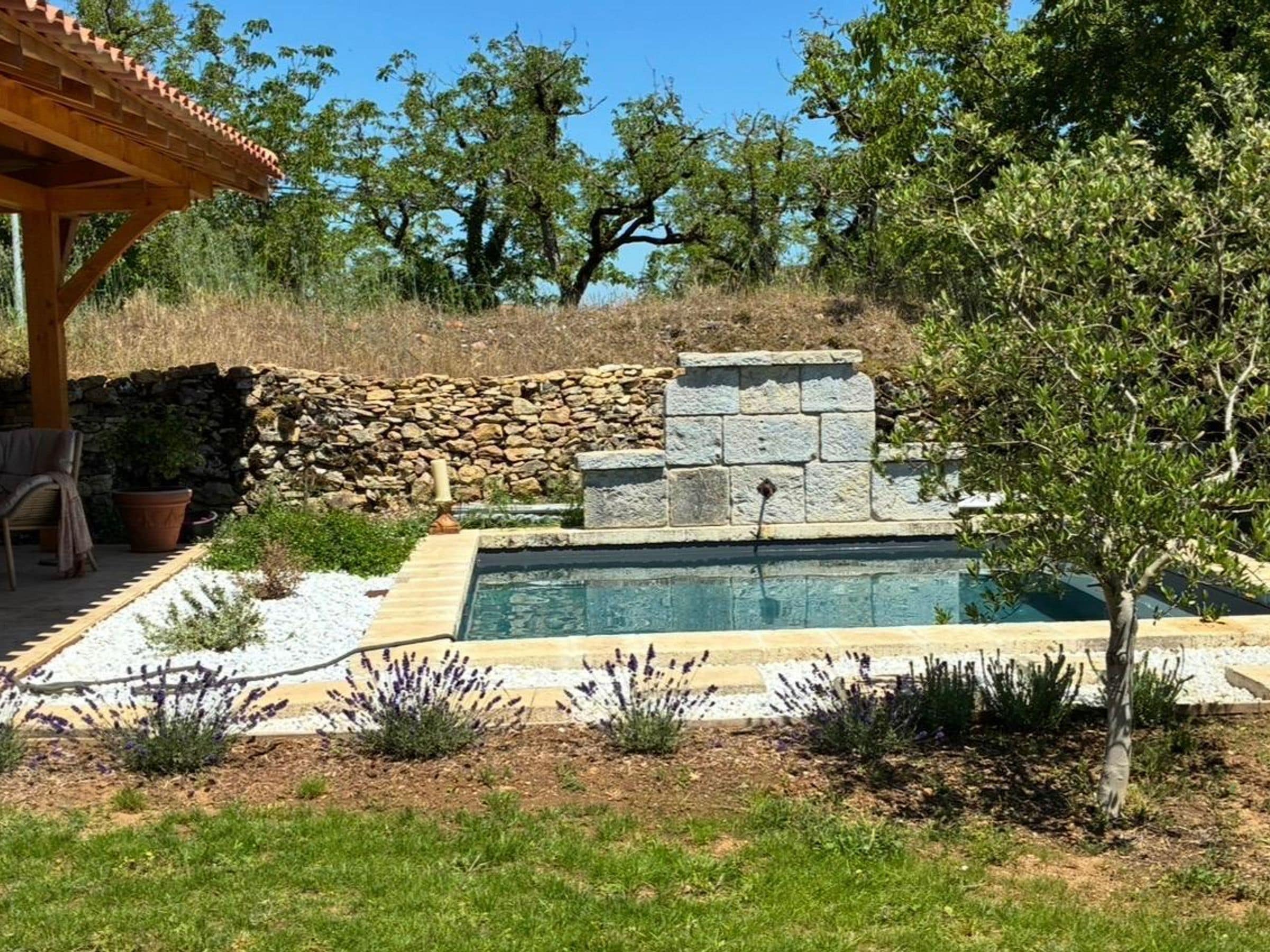 A swimming pool with a stone wall and a pergola.