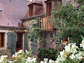 A stone building with a wooden balcony and a garden with white flowers. - Peaceful house with private pool and pets allowed (Florimont-Gaumier)