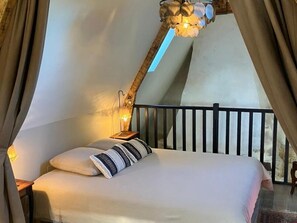 A bedroom with a bed, a nightstand, a lamp, and a view of the outside.