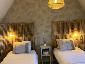 A room with two beds, each with a headboard, a bedside table with a lamp, and a wall-mounted light fixture.