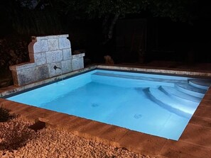 Une piscine rectangulaire bordée de pierres, avec un rebord en pierre muni d’une fontaine.