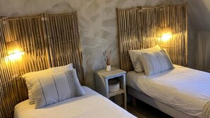 A room with two beds, each with a headboard made of vertical bamboo slats, a small bedside table with a lamp, and a wall with a textured pattern.