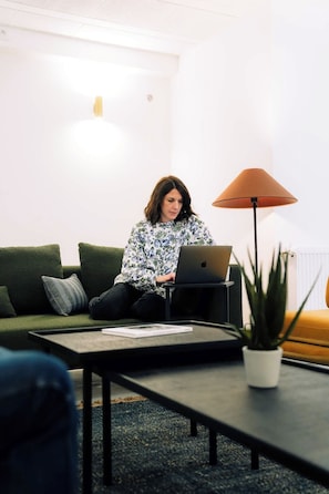 A person sitting on a green couch with a laptop, a small table with a plant, and a lamp. - Outsite Bordeaux - Work, Connect, Explore (Bordeaux)