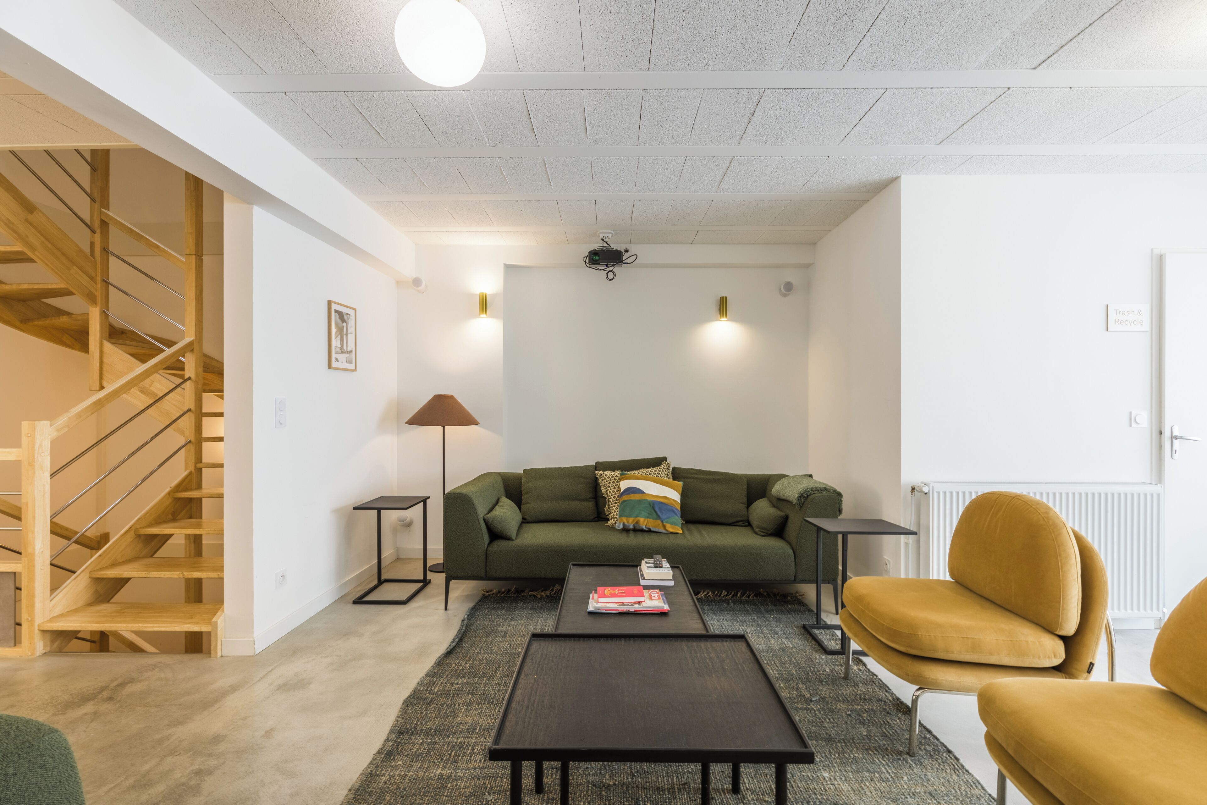 Una sala de estar moderna con una escalera, un sofá verde, una mesa de centro y un sillón amarillo.