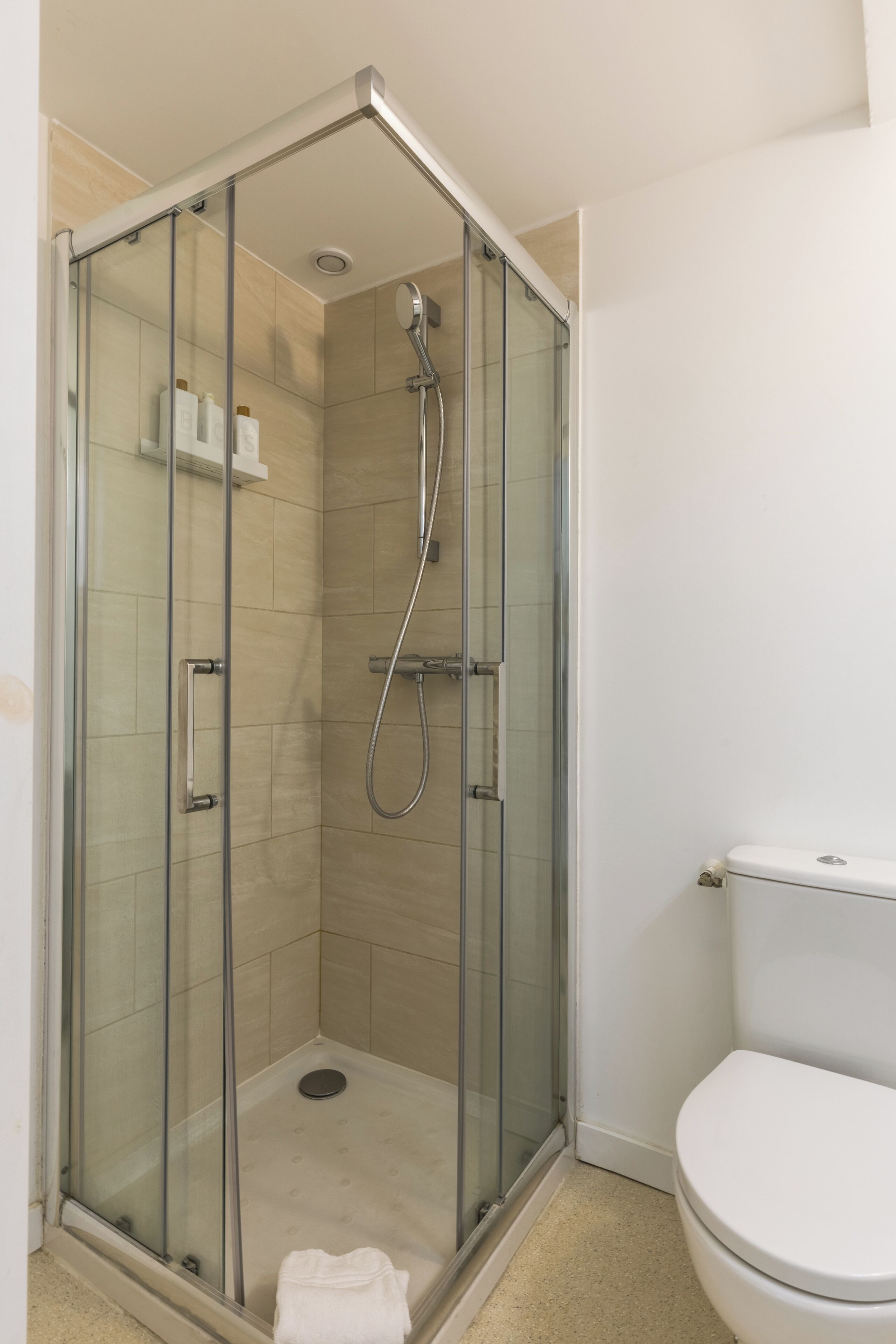 Cabina doccia con pareti in vetro, WC e mobile contenitore in un bagno.