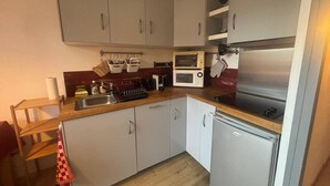 A compact kitchen with white cabinets, a stainless steel sink, a microwave, a toaster, and a refrigerator.