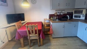 A compact kitchen with a dining table, chairs, a clock, a microwave, and a television.