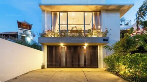 Une maison moderne à deux étages, dotée d’un balcon, de grandes fenêtres et d’une entrée bien éclairée.