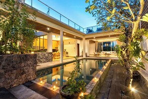 A modern outdoor pool area with a stone wall, wooden deck, and potted plants. - Maestro Bay View Villa by Premier Hospitality Asia (Nusa Dua)