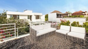 Une terrasse sur le toit, dotée de meubles en osier blanc, d’un sol en gravier et offrant une vue sur des bâtiments modernes.