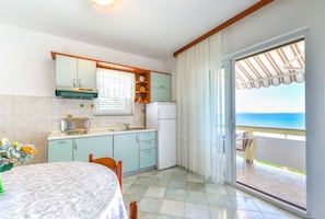 A kitchen with a dining table, a refrigerator, and a view of the sea through a sliding glass door. - Beachfront apartment Liverić 5 (Vir)