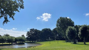 Um parque com lago, árvores e céu azul límpido.