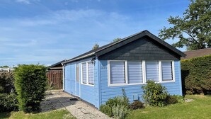 Uma pequena casa de um andar, azul, com telhado escuro, persianas brancas e um caminho de acesso de brita.
