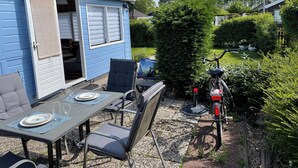 Um pátio com uma mesa posta para dois, uma cadeira e um edifício azul com porta de correr.