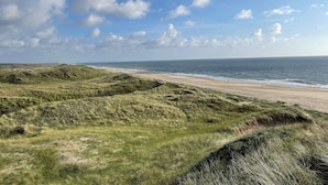 Paisagem costeira com dunas gramadas e uma praia.