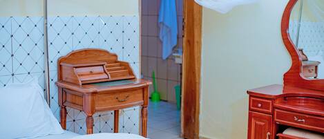 A bedroom with a wooden bed, a bedside table, a mirror, and a bathroom visible through an open door.