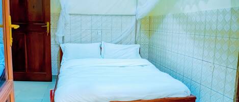 Una cama bien hecha con ropa de cama blanca en una habitación con paredes de baldosas y una puerta de madera.