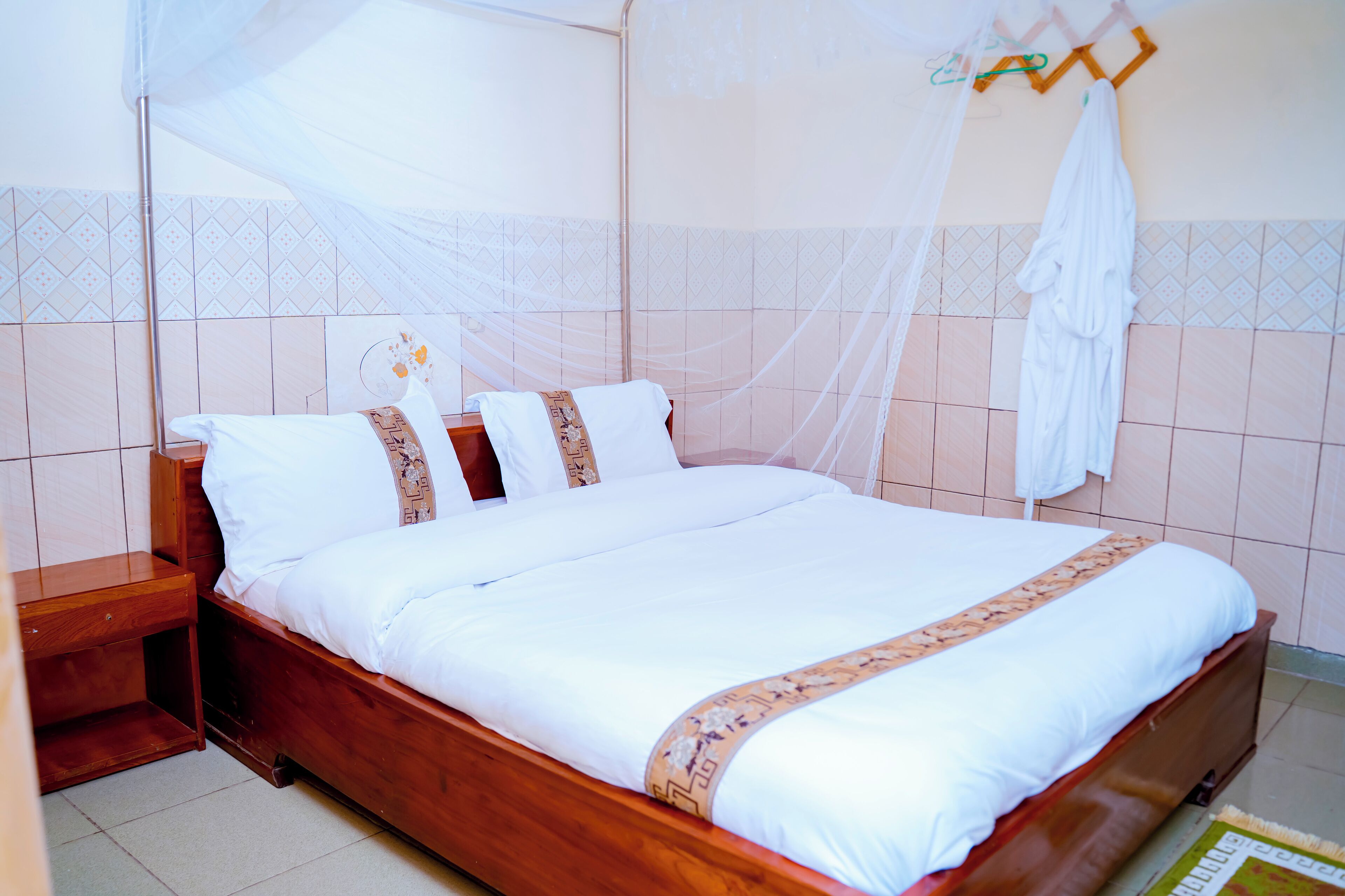 A neatly made bed with white linens and a decorative border, a wooden nightstand, and a mosquito net above the bed.